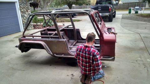 1985 Jeep CJ7 - A person works on a red Jeep CJ body that has been fitted with a custom roll cage.