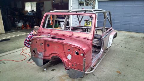 1985 Jeep CJ7 - A red Jeep CJ body, stripped down and fitted with a roll cage, is being worked on in a garage.