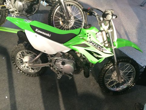 1987 Ford Bronco - A green Kawasaki dirt bike is displayed indoors, with another motorcycle partially visible in the background.