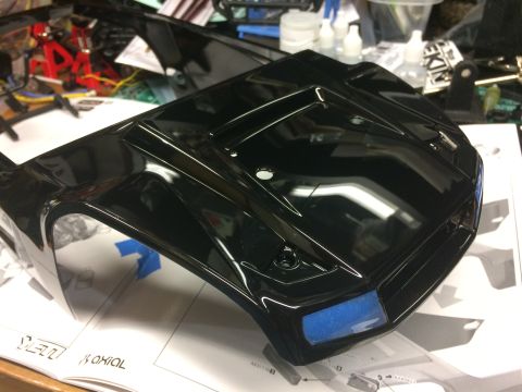 1989 Ford Bronco - A glossy black RC car body sits on top of assembly instructions, with blue tape covering the headlight areas.