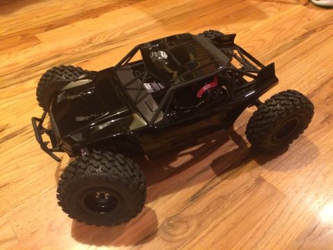 1989 Ford Bronco - A black remote control rock crawler sits on a wooden floor, its large tires and roll cage clearly visible.