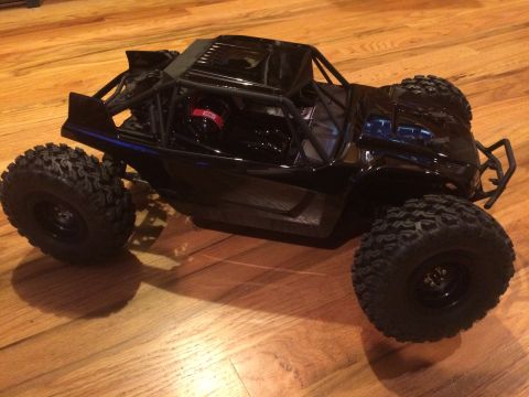 1989 Ford Bronco - This black remote control rock crawler features oversized tires and an exposed roll cage, sitting on a wooden floor.
