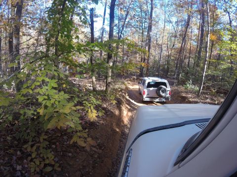 1979 Ford Bronco - A white 1979 Ford Bronco navigates a wooded trail, with another vehicle following closely behind.
