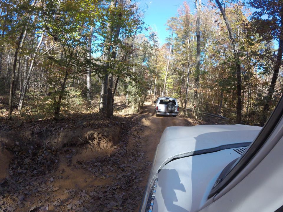 Two SUVs on a dirt road in a forest, one behind the other. Watermark 'SUPERMOTORS.NET' at bottom right