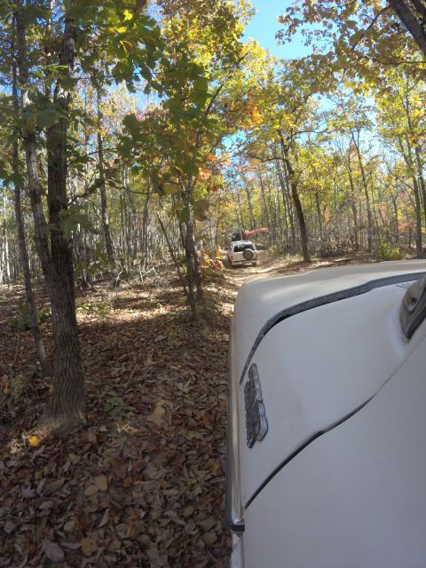 1979 Ford Bronco - Two SUVs navigate a dirt road through a forest during autumn.