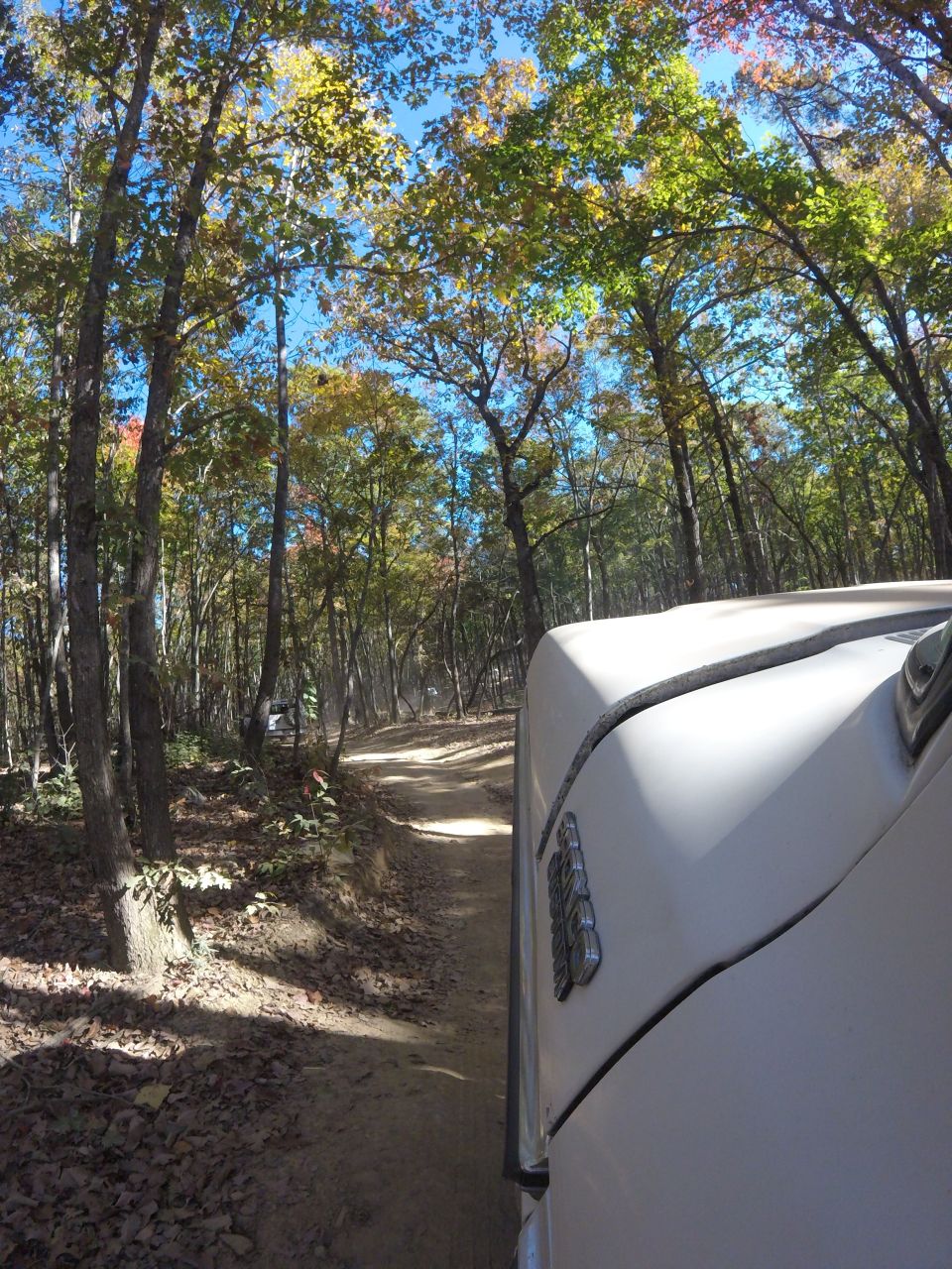 White 1979 Ford Bronco driving on a dirt road in a forest