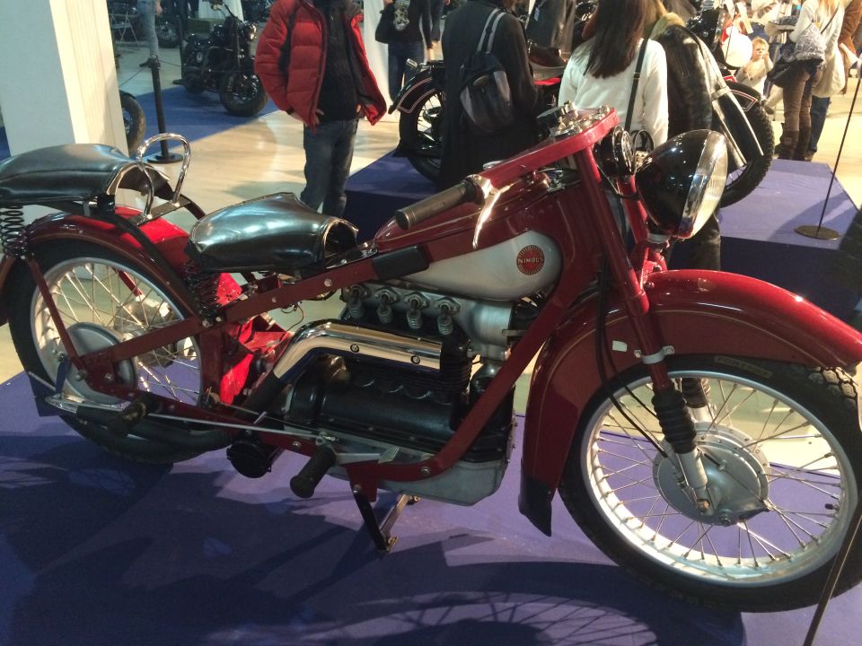 Red vintage motorcycle with a silver fuel tank and exposed engine cylinders, viewed from the side