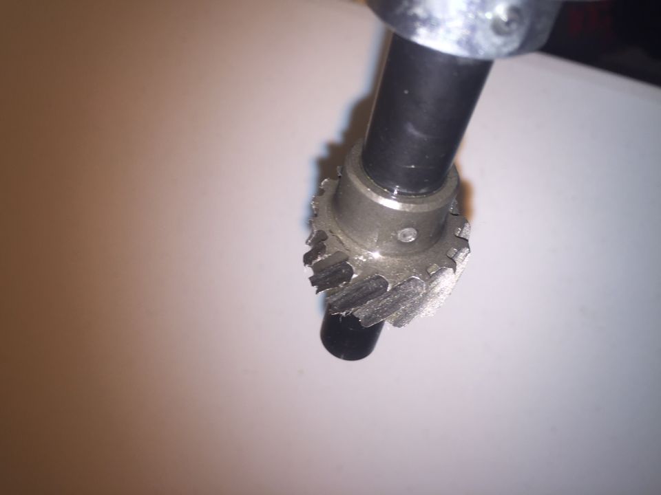 Damaged metal gear with broken teeth on a black shaft.
