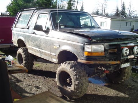 1993 Ford Bronco - Modified 1993 Ford Bronco with oversized tires and suspension lift sits in a yard.