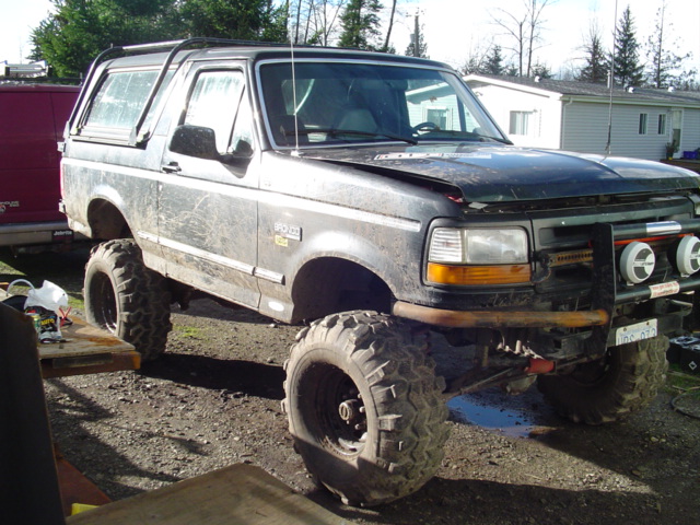 Muddy lifted black Ford Bronco front three-quarter view with tube bumper and lights
