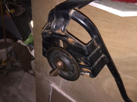 1967 Ford Custom Wagon - A rusty black metal automotive part, possibly a brake pedal assembly, is mounted against a wood-paneled wall. A threaded bolt with a wingnu…