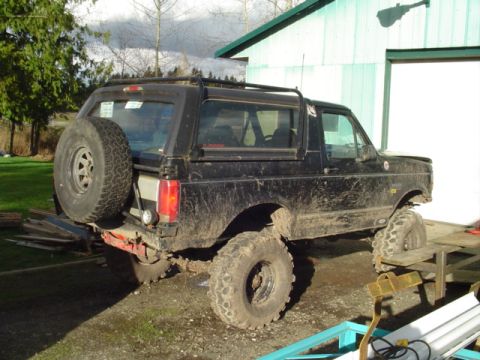 1993 Ford Bronco - This lifted black Ford Bronco is parked in a muddy yard next to a light blue garage.