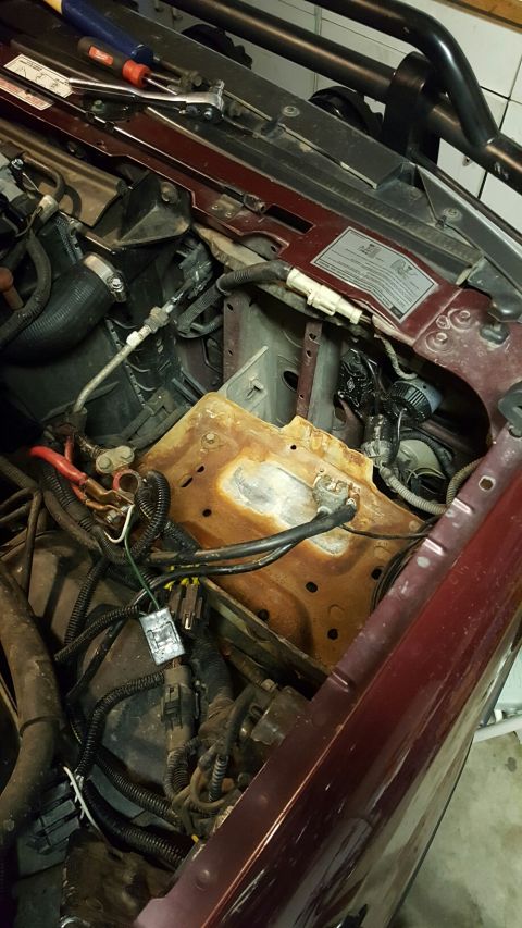 1996 Ford Bronco - The engine bay of a maroon Ford Bronco shows a rusty battery tray with red and black battery cables connected. Tools, including a ratchet a…