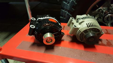 1996 Ford Bronco - A new black alternator with an orange logo sits next to an older, dusty gray alternator on a red surface. The alternators appear to be for…