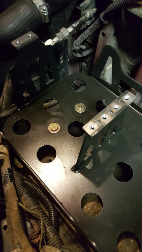 1996 Ford Bronco - A black metal bracket is being installed onto a vehicle's chassis with bolts. The bracket has multiple circular cutouts and is positioned n…