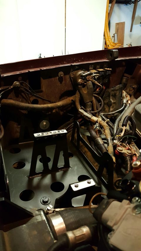 1996 Ford Bronco - A close-up view of the engine bay of a 1996 Ford Bronco, showing a custom black metal bracket installed with various wiring and hoses.