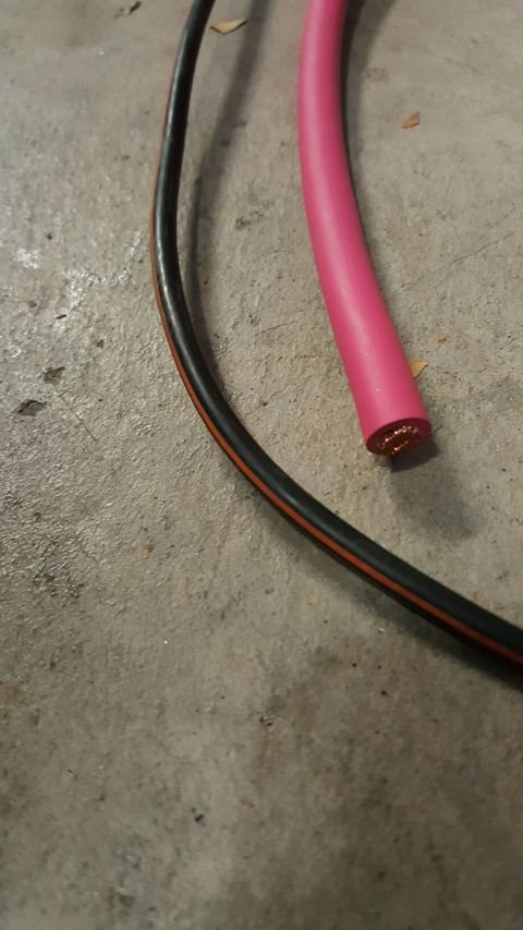 1996 Ford Bronco - A close-up view of a pink insulated wire and a black and orange striped wire lying on a concrete surface.