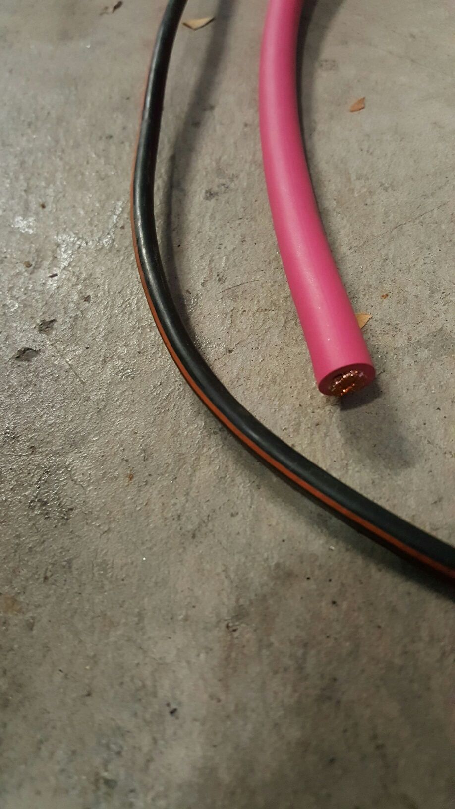 Pink insulated wire and black/orange striped wire on concrete