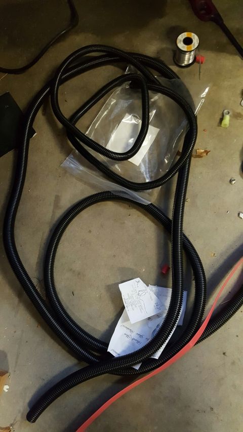 1996 Ford Bronco - A pile of black split loom tubing is coiled on a concrete floor, with a spool of solder and some receipts scattered nearby.