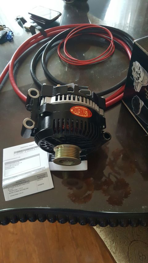 1996 Ford Bronco - A black Powermaster alternator is displayed on a dark, reflective surface, alongside red and black cables and a shipping document. The ship…