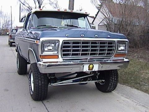 1995 Ford Bronco - This blue Ford truck, likely from the late 1970s, has a prominent chrome grille and visible aftermarket suspension components.