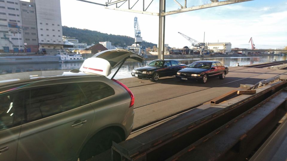Two black sedans parked by water, with a silver station wagon in the foreground.