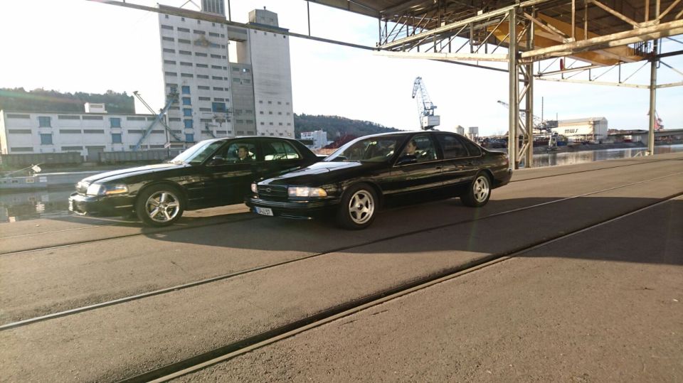 Two black sedans parked under an industrial canopy near a large building.
