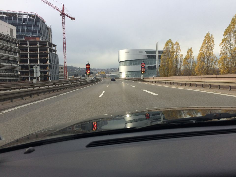 Vehicle dashboard and windshield view on a highway with reflections of buildings and traffic signs.