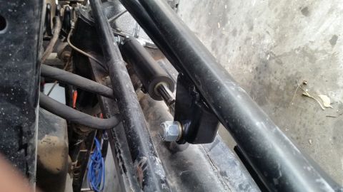 1979 Ford Bronco - A close-up view shows a black steering damper attached to the frame of a vehicle, secured by a silver nut and washer. The surrounding area…