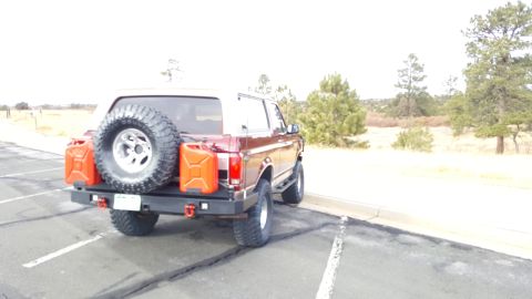 1996 Ford Bronco - The rear passenger side of a dark red Ford Bronco is shown parked in a lot with a spare tire mounted on the back, along with two orange jer…