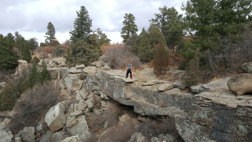 Person standing on a rocky ledge in a wooded canyon.