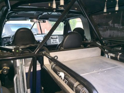 1986 Ford Bronco - The interior of a modified vehicle, likely a truck or SUV, is shown from the rear passenger perspective. A roll cage, racing seats, and a m…