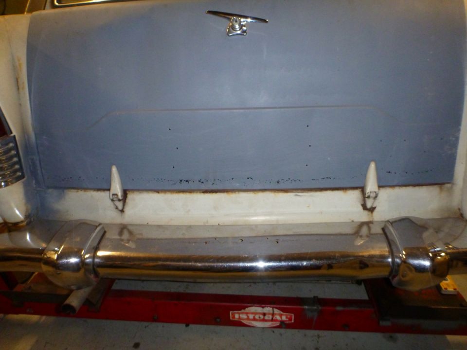 Rear view of a classic car with chrome bumper and light blue trunk lid.