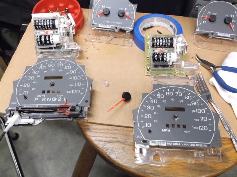 Disassembled car instrument cluster parts including speedometers and odometers on a table.