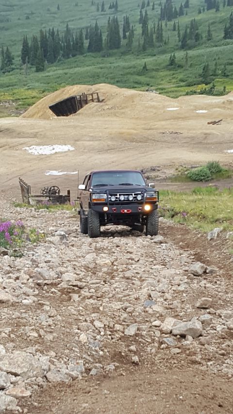 1996 Ford Bronco - A dark-colored Ford Bronco is parked on a rocky, off-road trail with a mine entrance and tailings pile in the background.