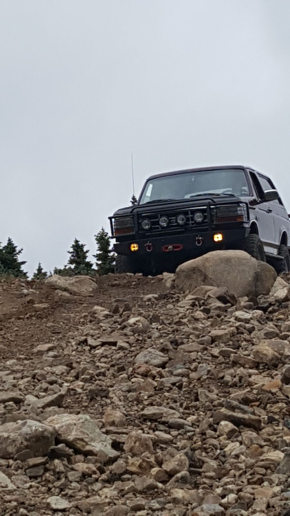 Dark Ford Bronco on a rocky trail with aftermarket bumper and lights.