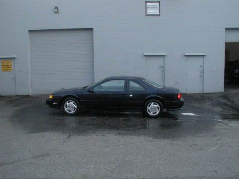 1990 Ford Thunderbird - A side view of a black 1990 Ford Thunderbird parked outside a commercial building.