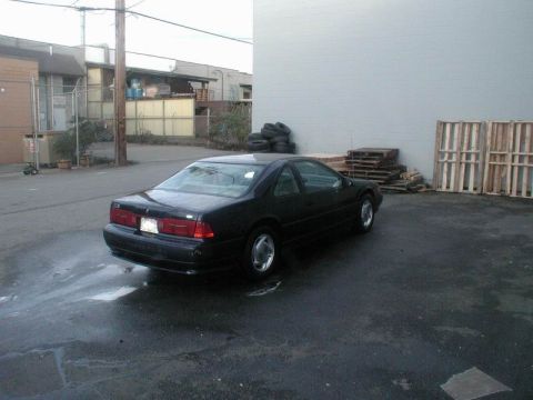 1990 Ford Thunderbird - Black 1990 Ford Thunderbird coupe parked in an industrial area with pallets and tires nearby.