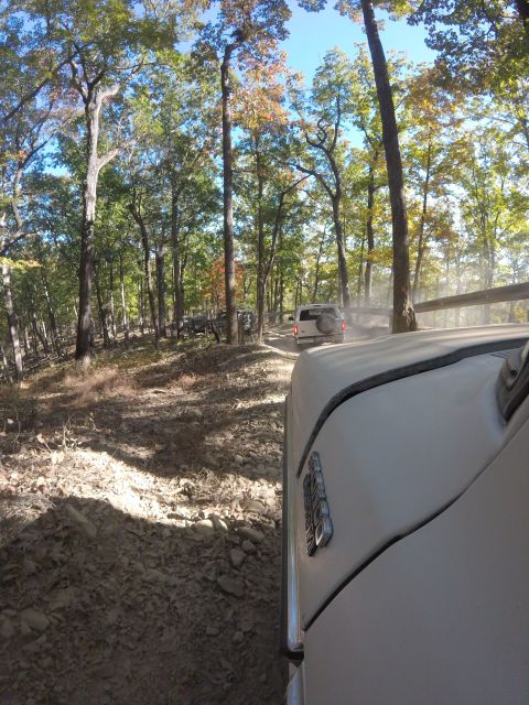 1979 Ford Bronco - A white SUV drives down a dusty, wooded trail. The perspective is from another vehicle, showing the side of its white body and a portion of…