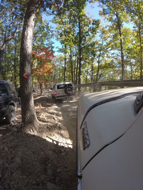 1979 Ford Bronco - A white Ford Bronco is driving on a dirt trail through a forest, followed by another vehicle. The photo is taken from the perspective of a…