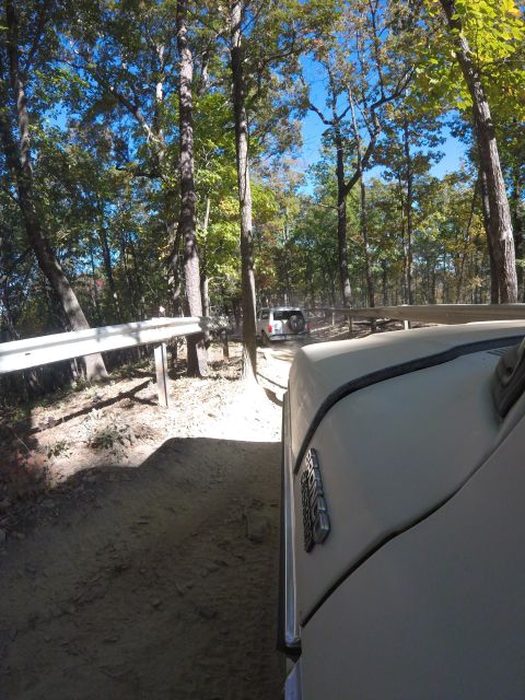 1979 Ford Bronco - A light-colored vehicle, possibly a Ford Bronco based on the visible emblem, drives down a dirt path surrounded by trees. Another white SUV…