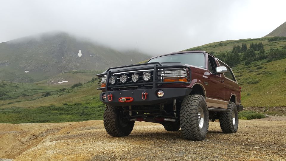 Lifted maroon 1996 Ford Bronco with aftermarket bumper and grille guard in foggy mountains.