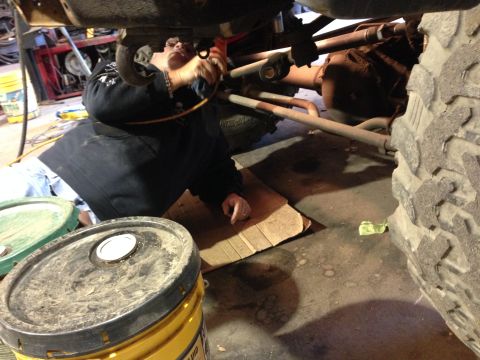 1979 Ford Bronco - A person works underneath the chassis of a vehicle, which appears to be a truck or SUV, with large tires and suspension components visible.…