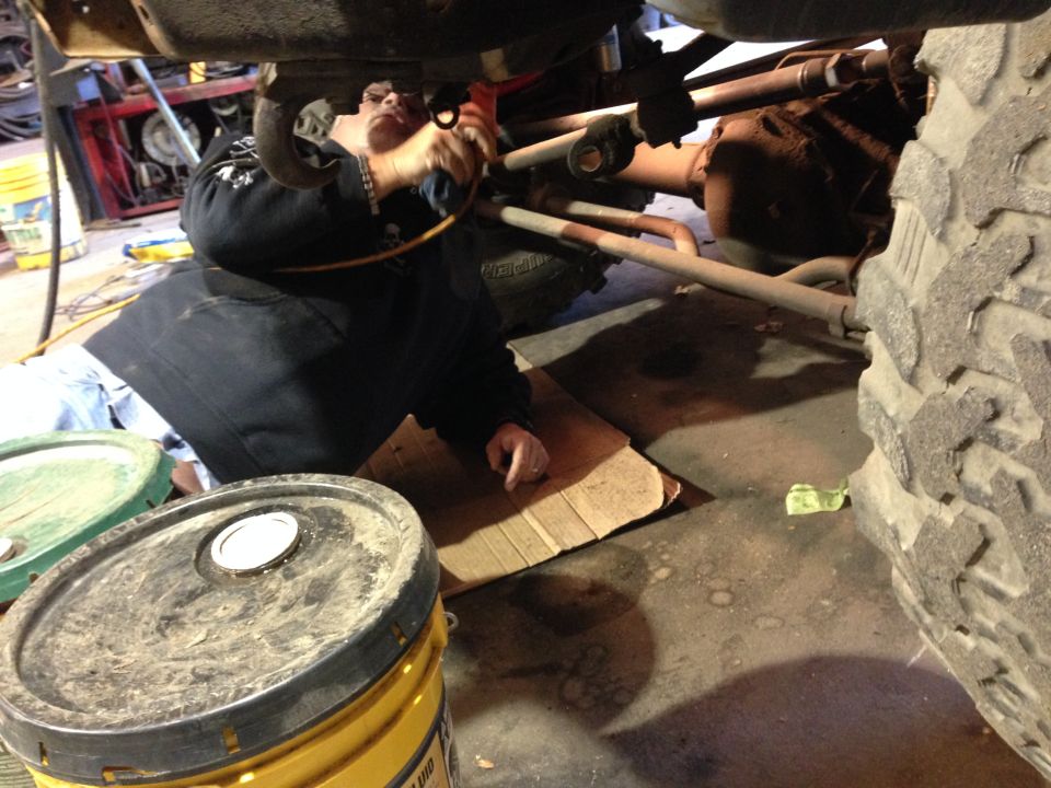 Person working under a large vehicle, with tires and buckets in foreground.