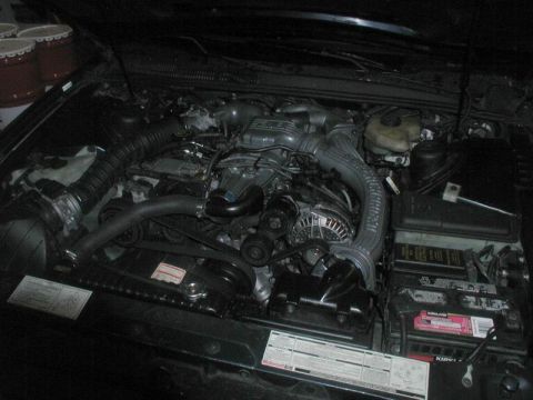 1990 Ford Thunderbird - The engine compartment of a vehicle is shown, various engine components and a battery.