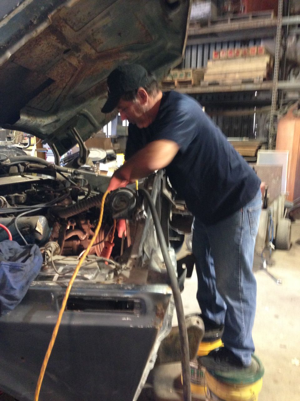 Man working on car engine, standing on buckets.