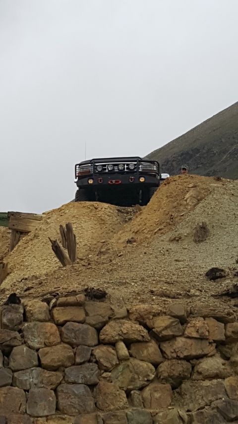 1996 Ford Bronco - A black Ford Bronco with a brush guard is parked on a dirt hill with a rocky wall in the foreground. A person wearing a hat is visible behi…