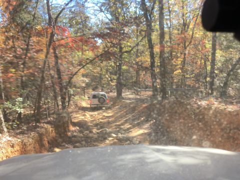 1979 Ford Bronco - A white SUV navigates a rocky, off-road trail through a forest with autumn foliage. The vehicle is viewed from the perspective of another v…
