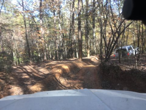 1979 Ford Bronco - A white SUV is parked on a dirt trail in a wooded area during the fall. The vehicle is viewed from the perspective of another vehicle drivi…