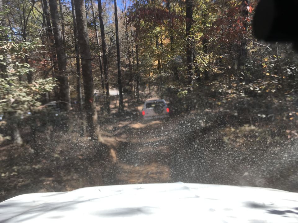 White SUV driving on a muddy road through a forest in autumn.